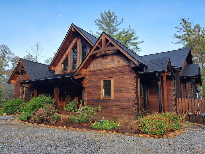 Photo of a log cabin with plank logs. The home's entrance is under a covered porch and a geometric window dormer is over the front entrance