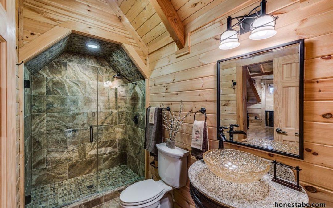 Photo of stone geometric shower and glass raised sink system in an exposed wood walls and ceiling room of a log home