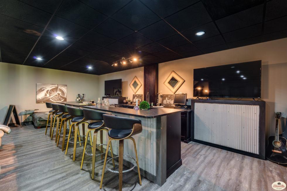 Photo of a bar area with double tv's against the wall. The floors are a light wood and the ceiling is dark stained wood