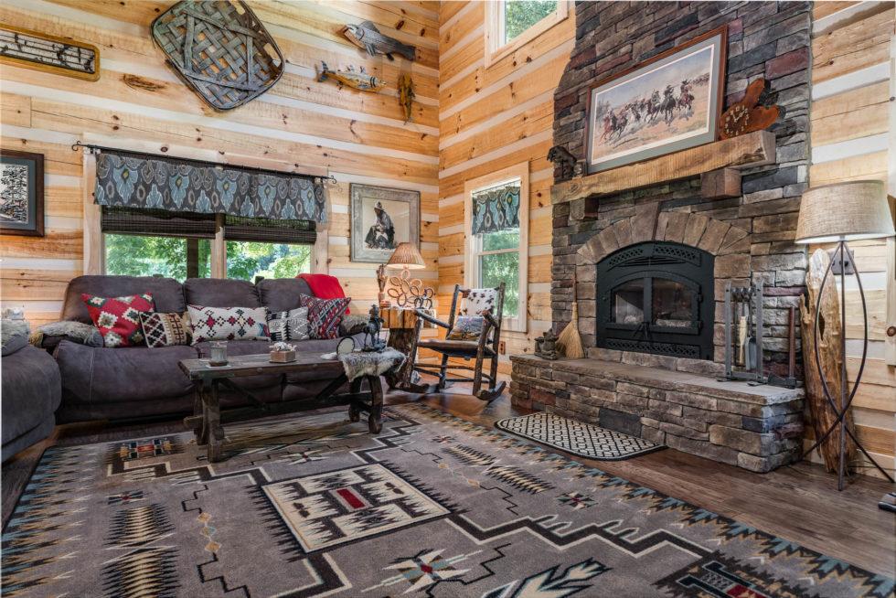 Photo of interior great room with wide plank log home walls, soaring ceiling and wood floor framing a stone two story fireplace