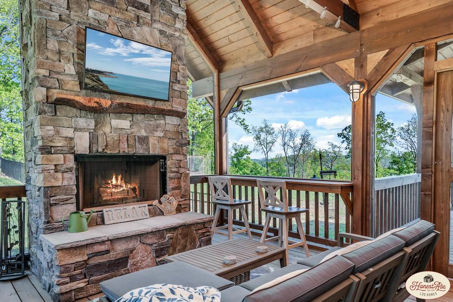 Photo of screened porch with stone fireplace and a large screen tv for the mantle. The porch has bar seating against the screen. The porch ceiling is exposed wood