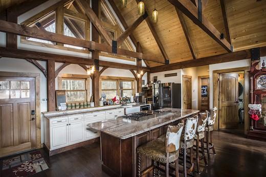 Photo of log cabin with cozy kitchen and eat-in bar space. the a-frame ceiling supports are slightly darker than the honey colored exposed wood ceiling.