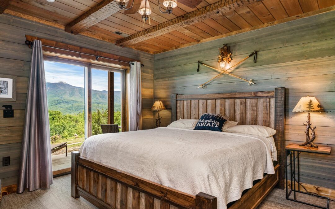 Photo of bedroom with exposed wood wall painted green and brown wood exposed ceiling and floors. the exterior wall has a sliding glass door leading to an outdoor deck